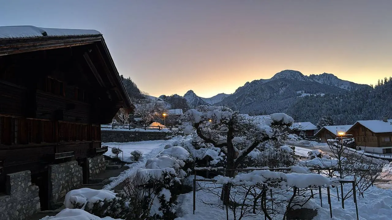 Arbres chargés de neige devant les chalets et les montagnes au crépuscule