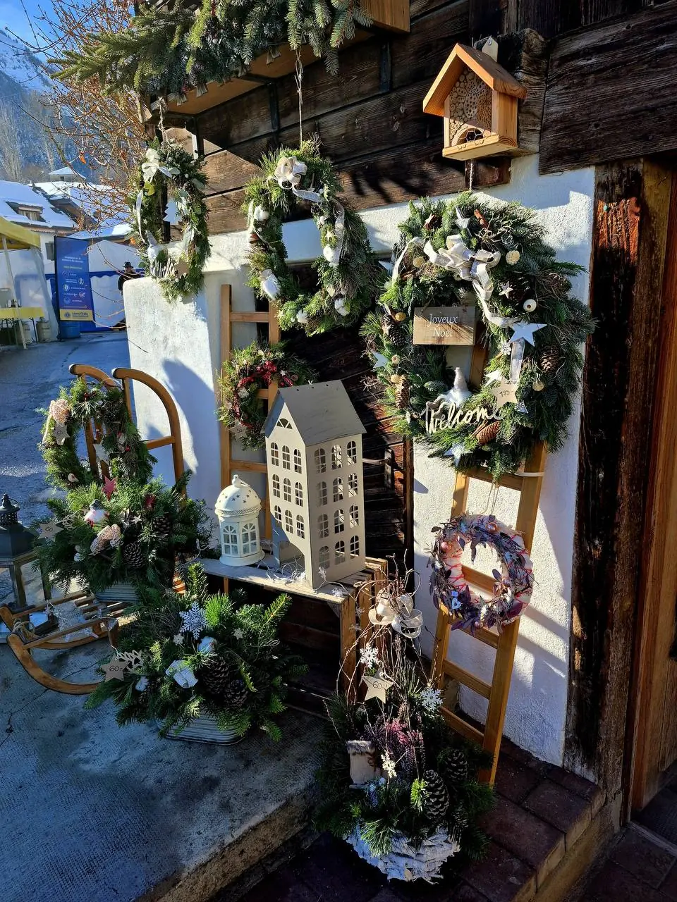 Couronnes de Noël, lanternes et décorations devant une façade en bois, en plein jour